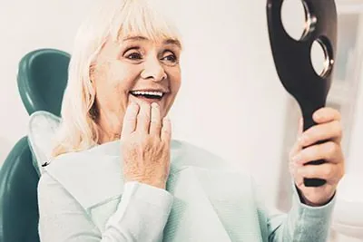 woman loving her look in the mirror after getting dentures at Ember Dental Arts